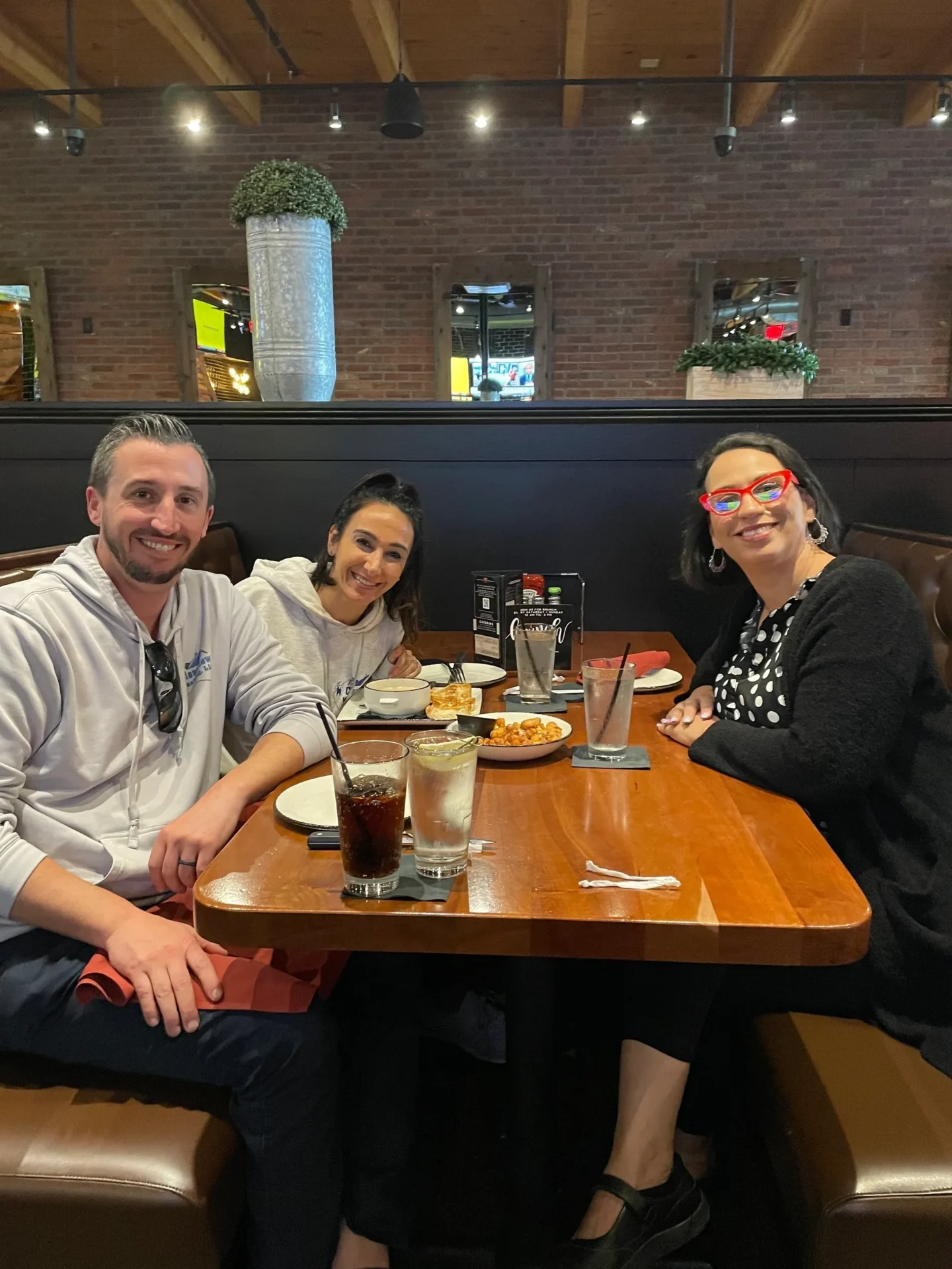 Three people sitting at a table with drinks and food.