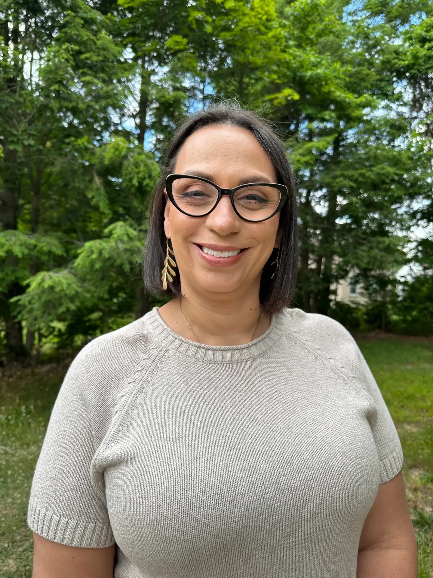 A woman wearing glasses standing in front of trees.