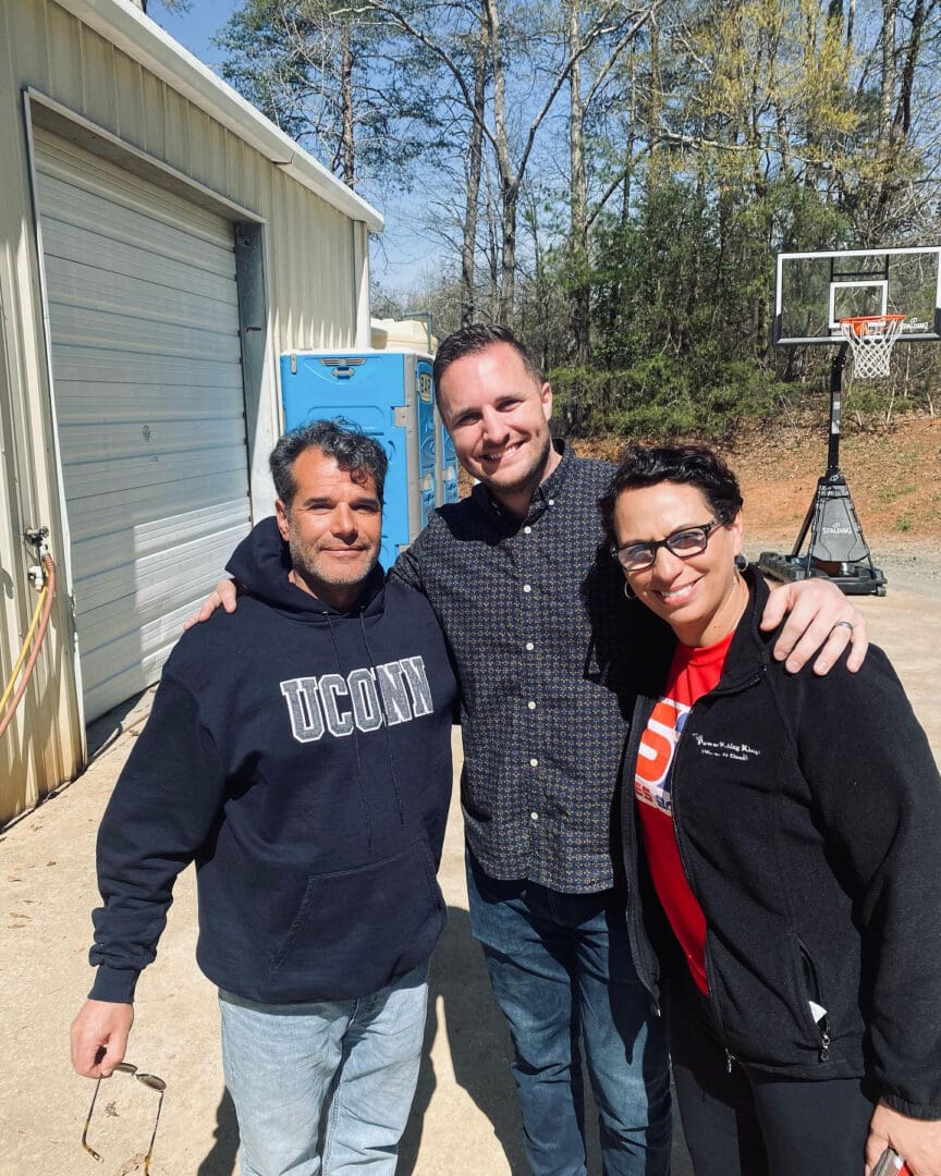 Three men standing next to each other in front of a basketball hoop.