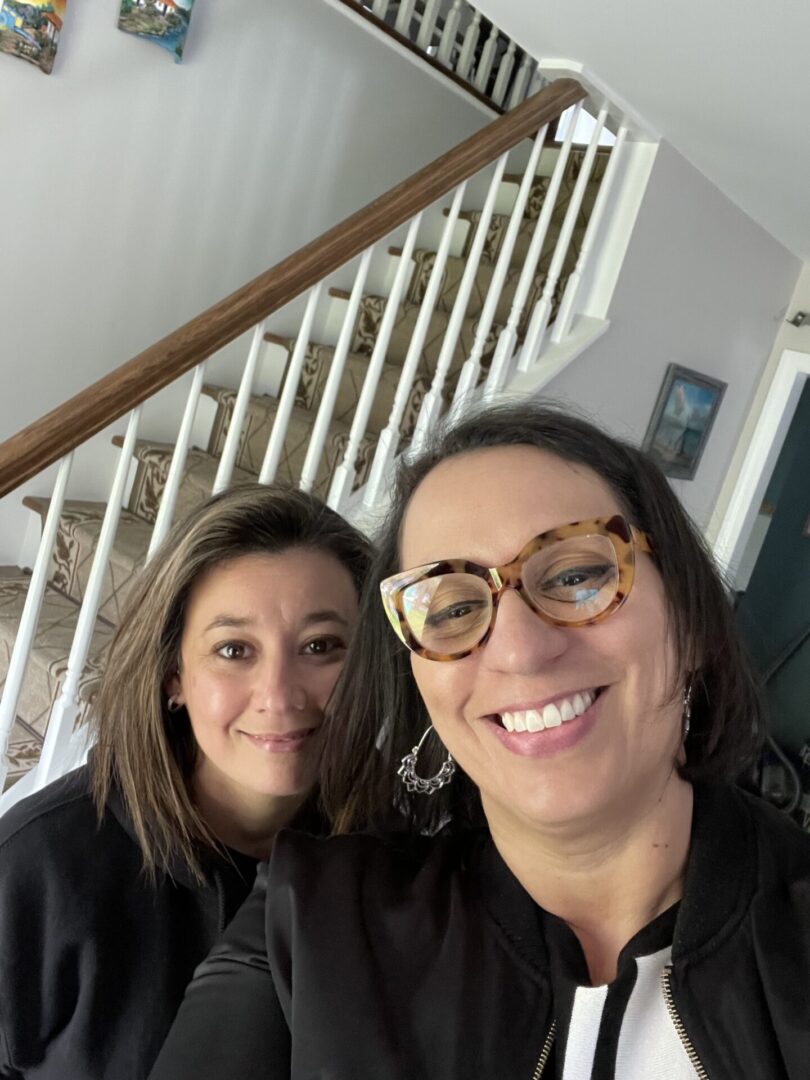 Two women smiling for a picture in front of the stairs.